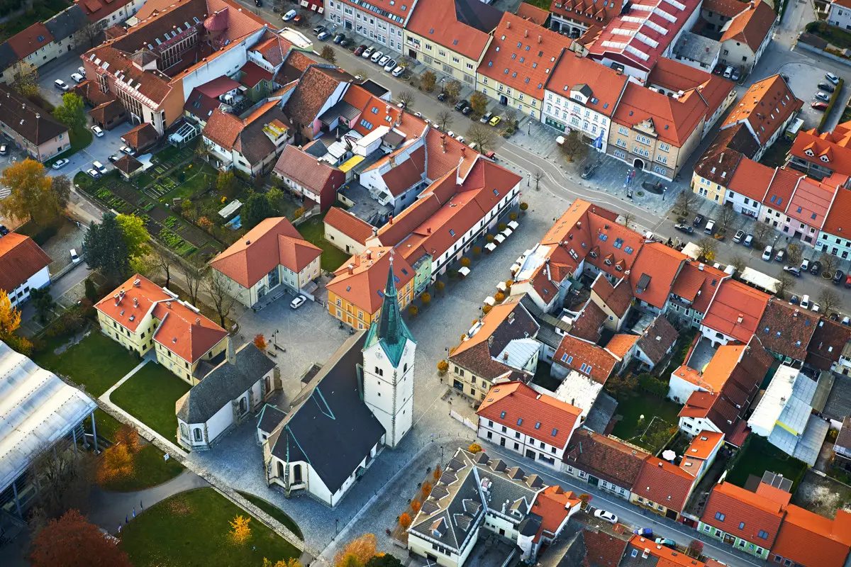 Aerial view of a European town square with red-roofed buildings and a church with a tall steeple.