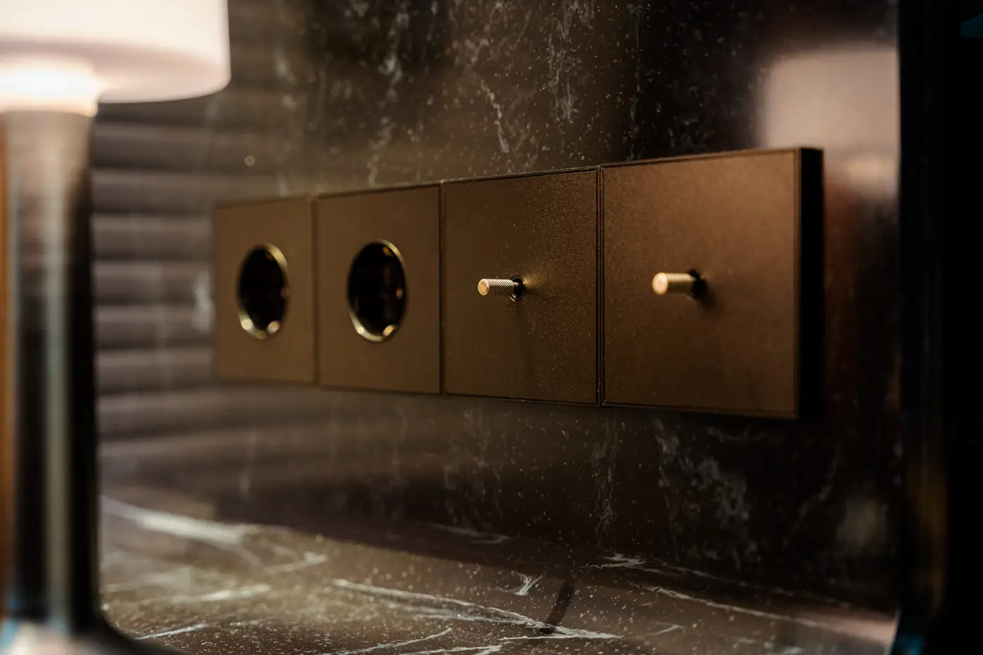 Close-up of four black wall switches including two power sockets and two toggle switches on a dark marble wall.