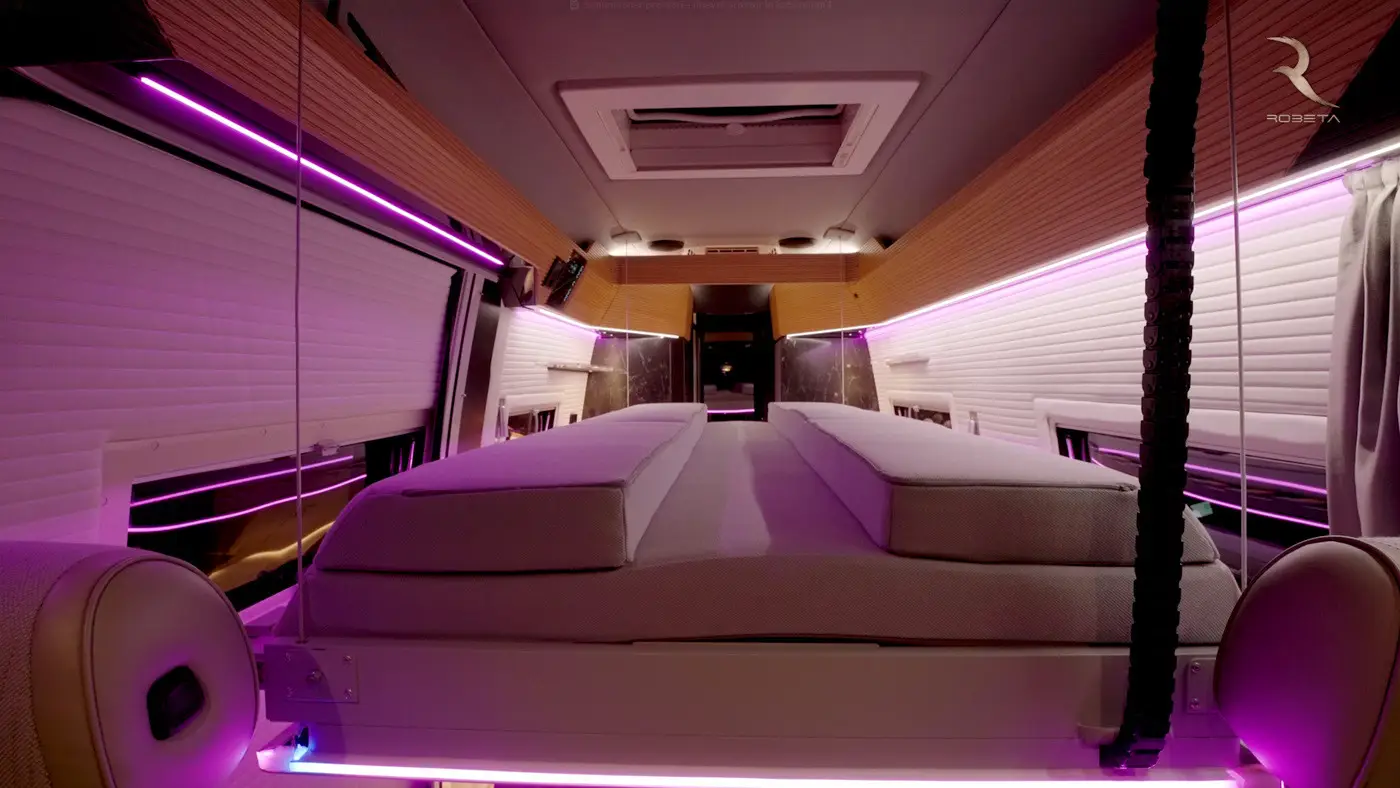 Modern camper van interior with a raised bed framed by purple LED lights and wooden accents.