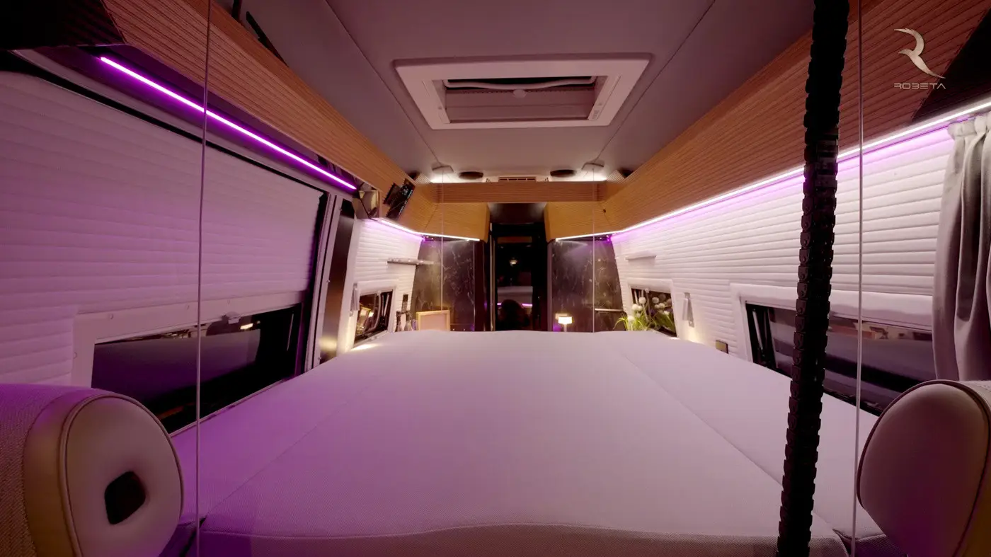 Modern camper van interior with a spacious bed, wood accents, and purple LED strip lighting.