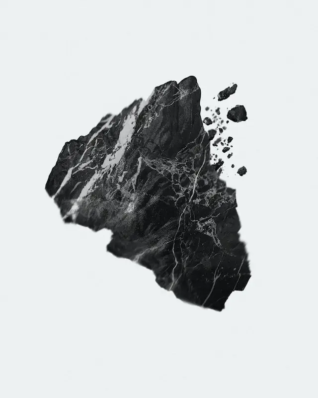 Black rock with white veining breaking apart into smaller fragments on a white background.